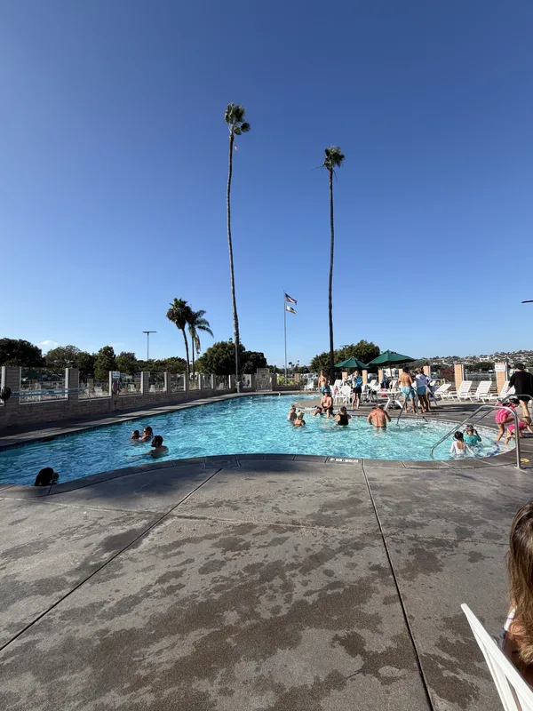 The swimming pool at Mission Bay RV Resort in San Diego, swimmers in the water and tall palms against a deep blue sky