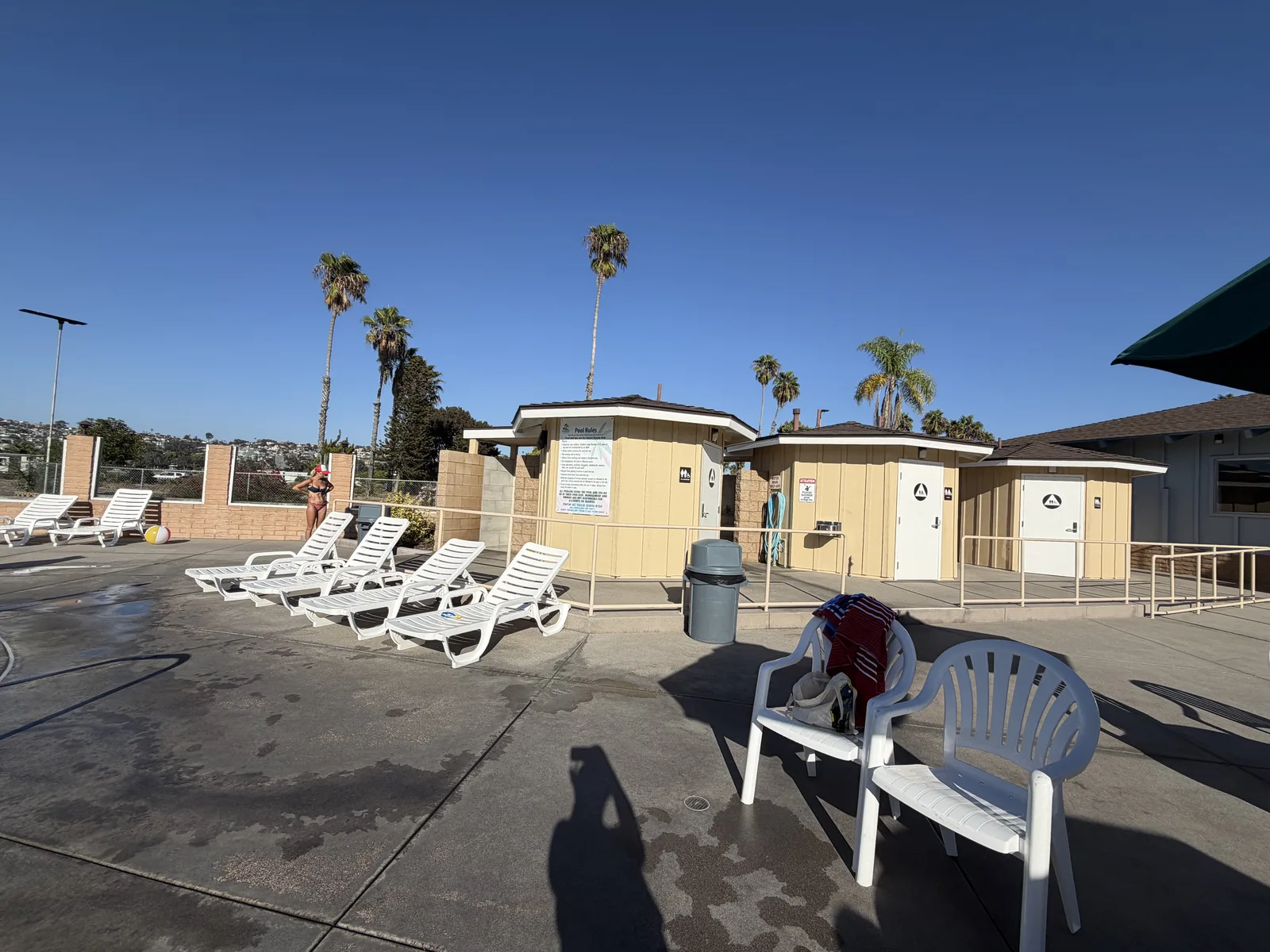 The pool deck at Mission Bay RV Resort, white loungers lined up beside the restroom and shower building under the palms