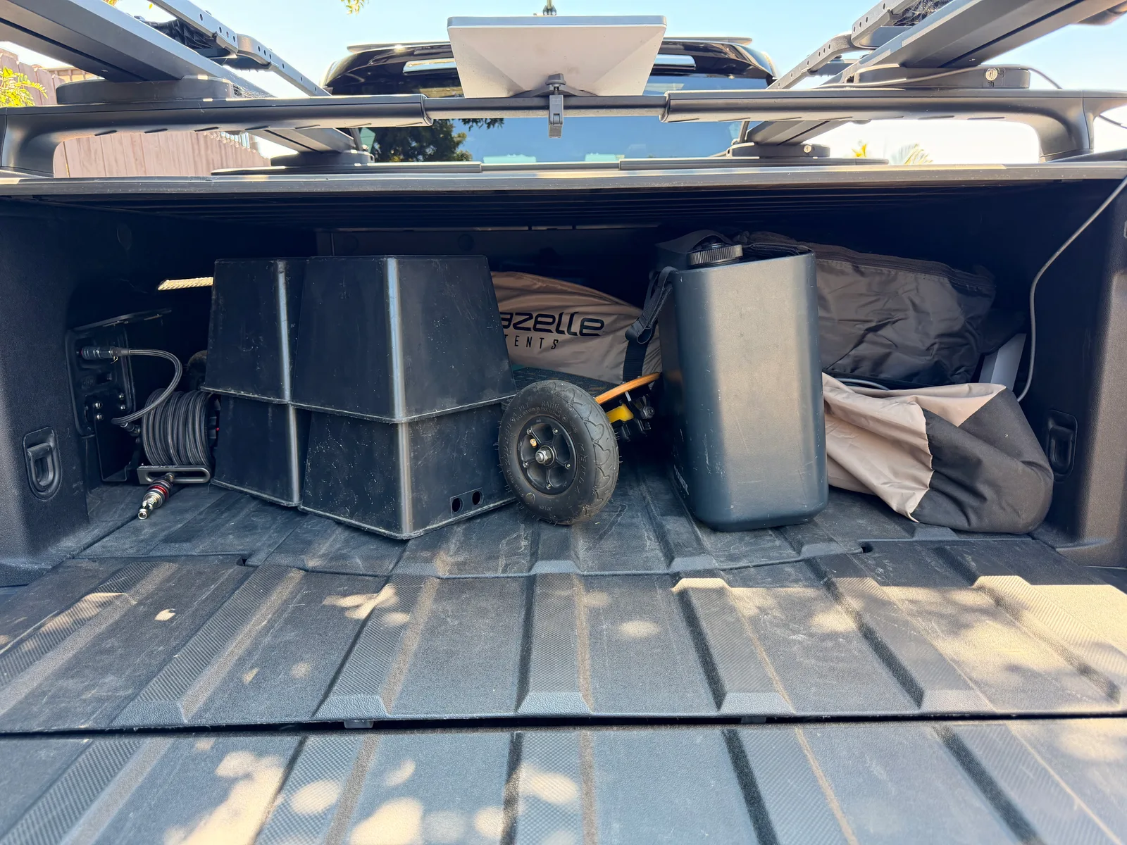 The Rivian R1T's compact bed packed tight with a Gazelle gazebo bag, an electric skateboard, tools, folding tables, a portable power station, and camping gear