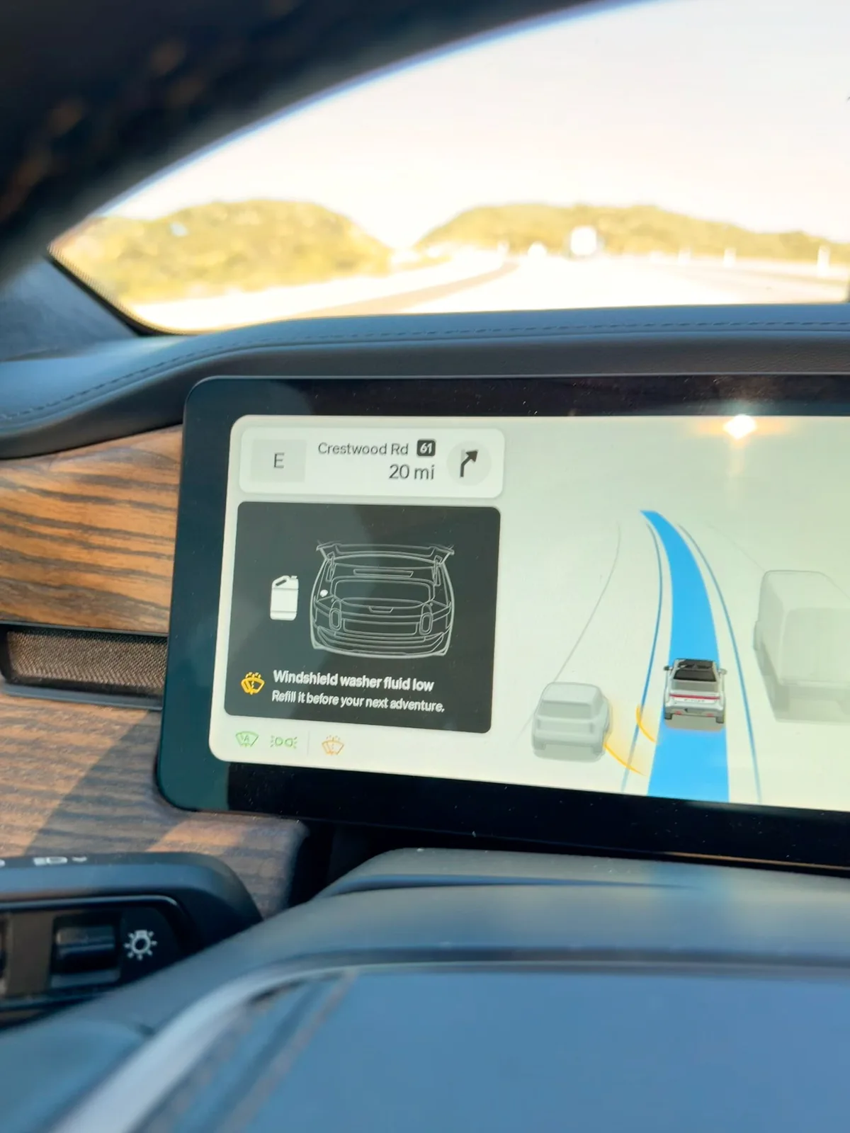 The Rivian R1T's center display mid-drive on I-8 with the navigation showing 20 miles to the Crestwood Rd exit and a "Windshield washer fluid low" alert overlaid