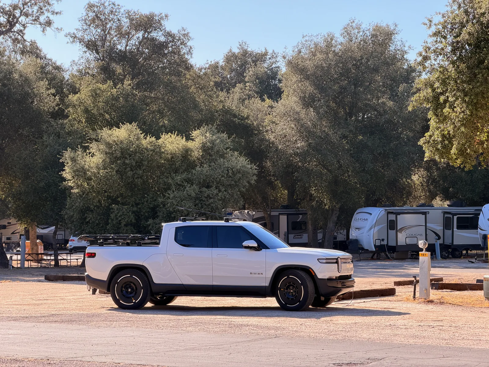 The white Rivian R1T parked at the Boulevard KOA campsite under California oaks, with a fifth-wheel trailer visible at the neighboring site