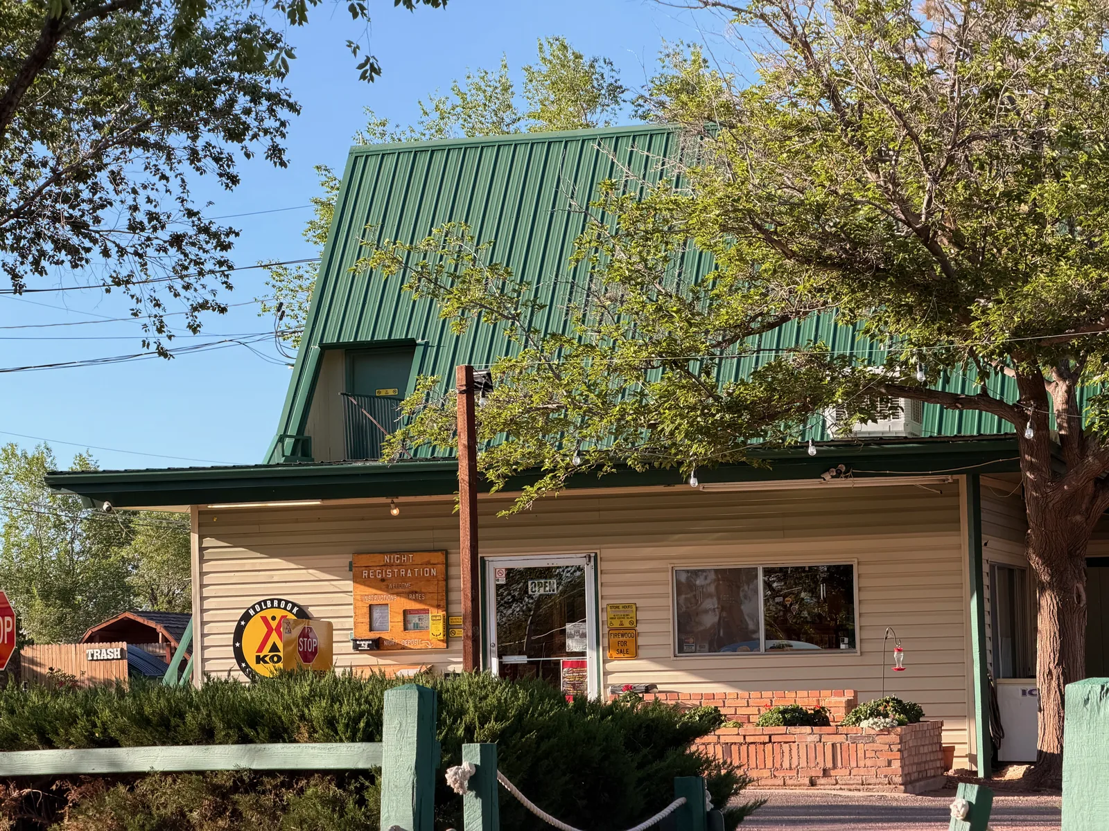 The Holbrook KOA office, a green-roofed wooden cabin with rust-painted siding, surrounded by trees and a small parking area