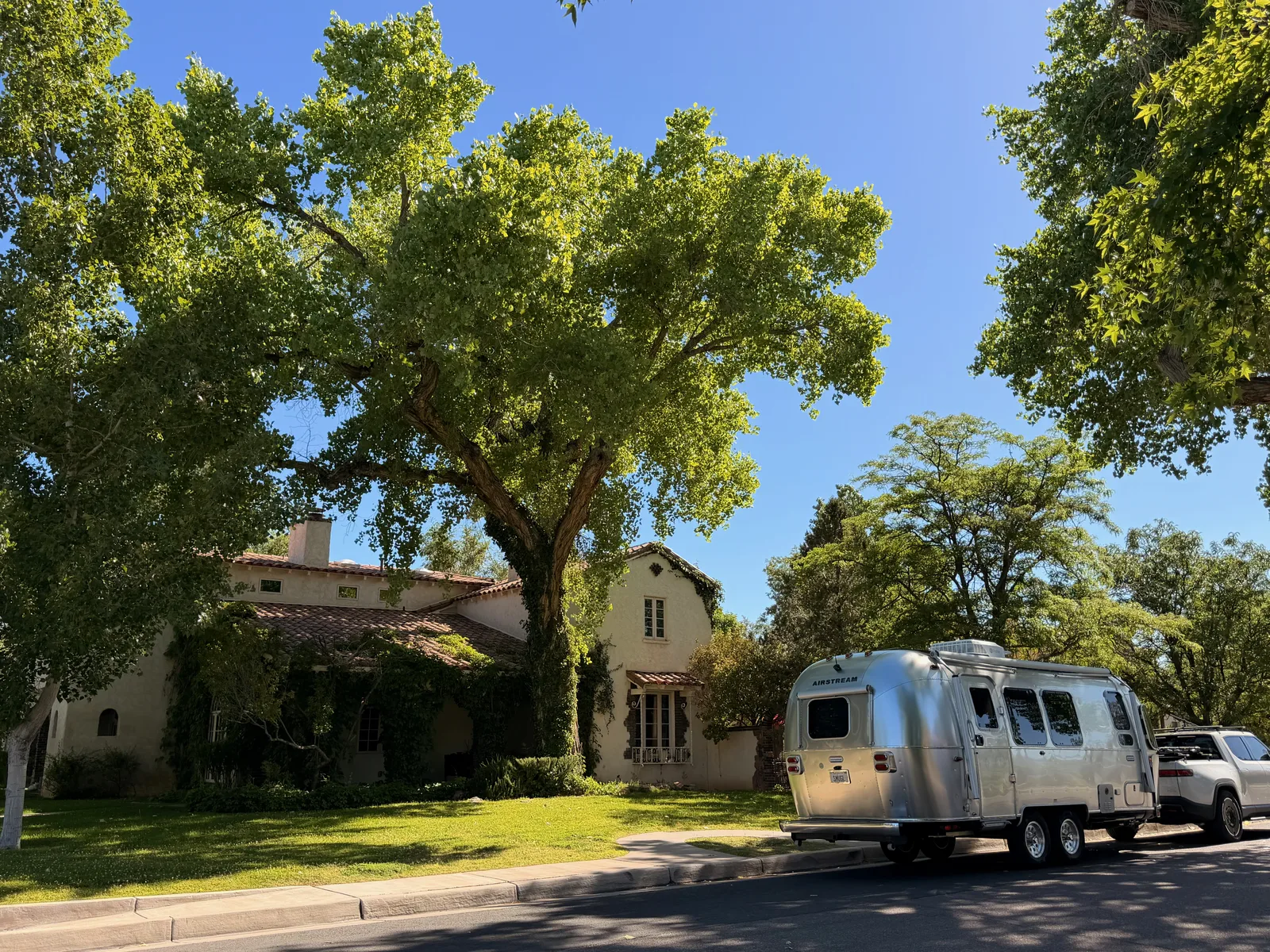 The Jesse Pinkman house at 322 16th St SW, a Spanish Revival single-story with stucco walls, terra-cotta tile roof, and ivy on the side, with the rear of the silver Airstream parked at the curb at right edge