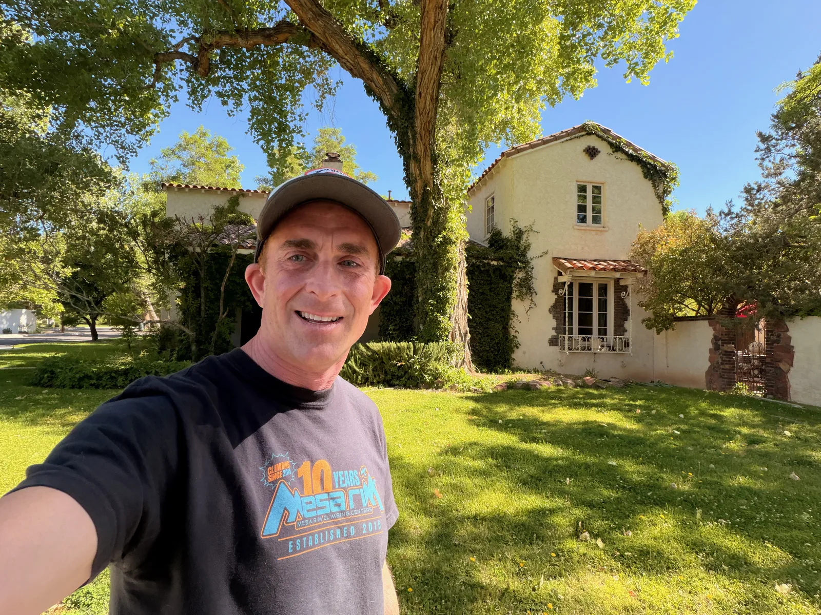 Closer selfie in front of the Jesse Pinkman house, Eric smiling under a green ball cap, the Spanish Revival exterior with ivy and bay windows clearly visible
