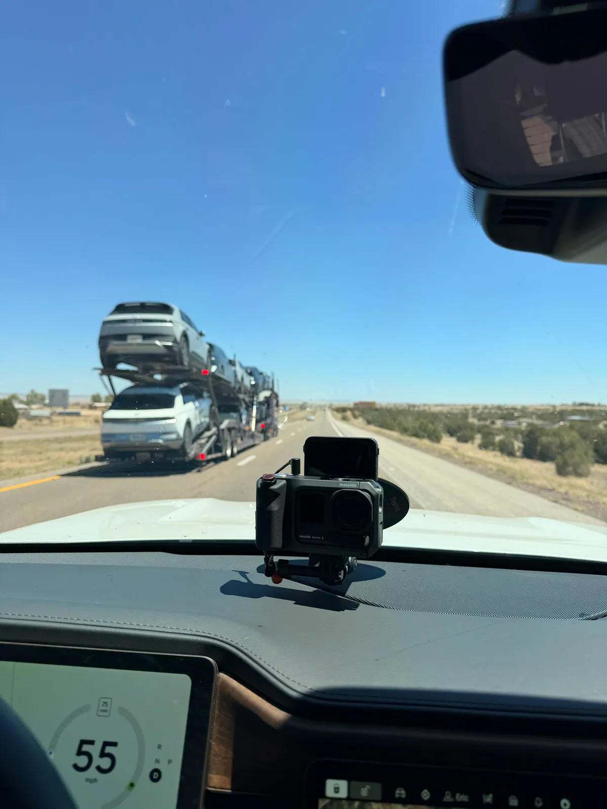 View from the Rivian R1T driver seat on I-40 east at 1:49 PM, an action camera mounted on the dashboard, the rig holding 55 mph in a 75 mph zone, a double-decker car-hauler truck in the next lane carrying a load of new Hyundai Ioniq 5 EVs being delivered east