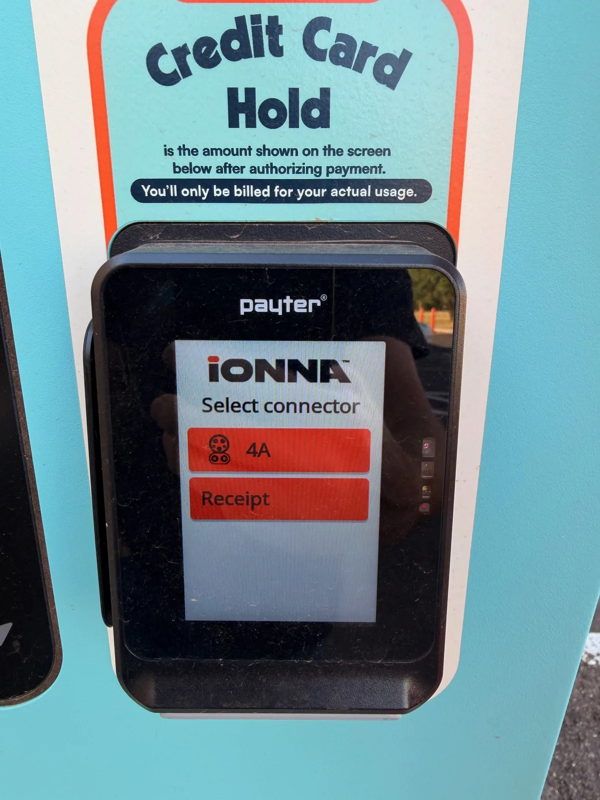 The Payter credit-card terminal mounted on the IONNA pedestal showing the "Select connector" screen with stall 4A in red and a Receipt option, under an instructional "Credit Card Hold is the amount shown on the screen below after authorizing payment, you'll only be billed for your actual usage" sign