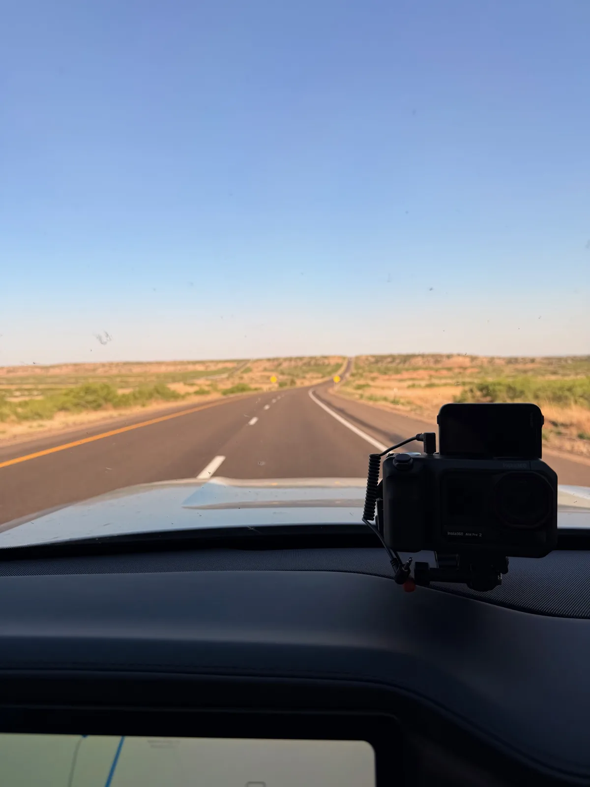 Through-the-windshield view eastbound on I-40 east of Tucumcari at 6:05 PM, the road curving gently through the high-desert mesa country, the action camera mounted on the dash, sage-and-sandstone landscape stretching to the horizon under a deep blue late-afternoon sky
