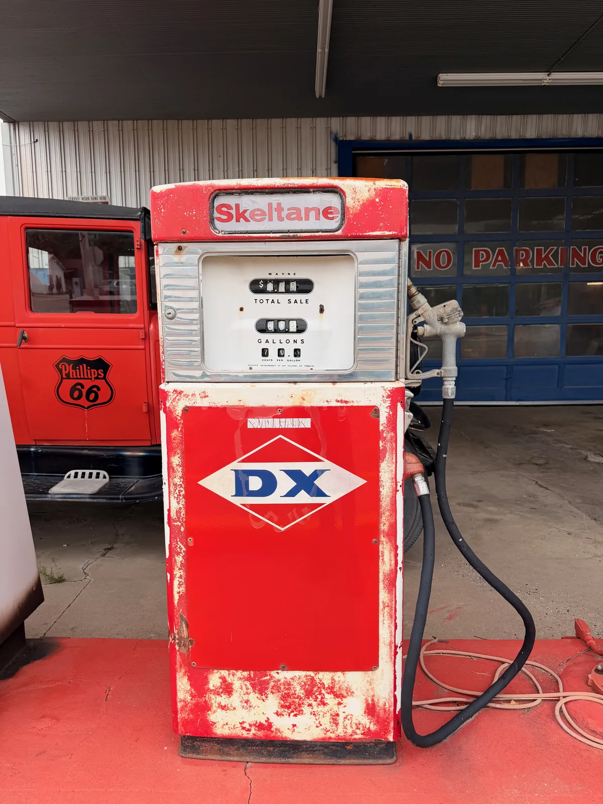 A vintage red DX-brand gas pump on the red-painted platform outside Hometown Coffee, chrome trim and the round DX logo on the face, the corner of the Phillips 66 truck and a fire extinguisher visible alongside