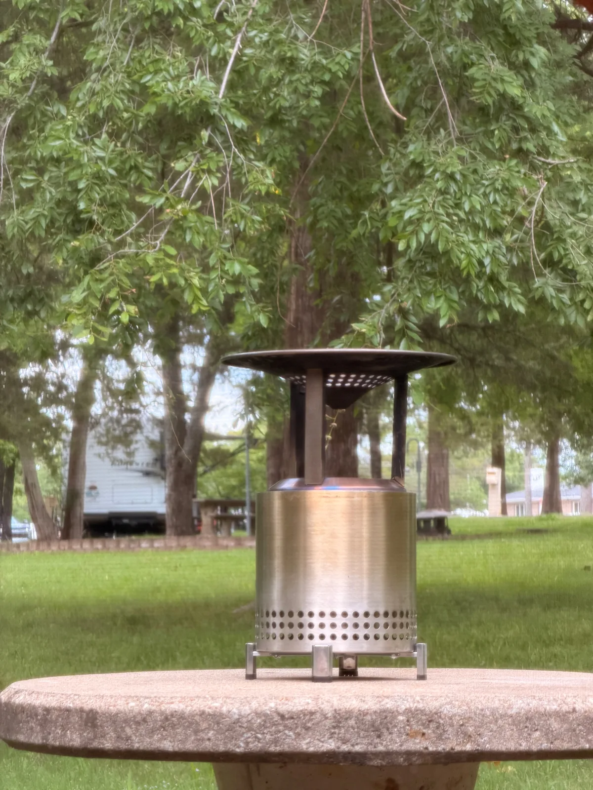 The stainless-steel Solo Stove fire pit glowing with flames on the picnic table at the Indian Point campsite at dusk, the lake visible behind through the trees