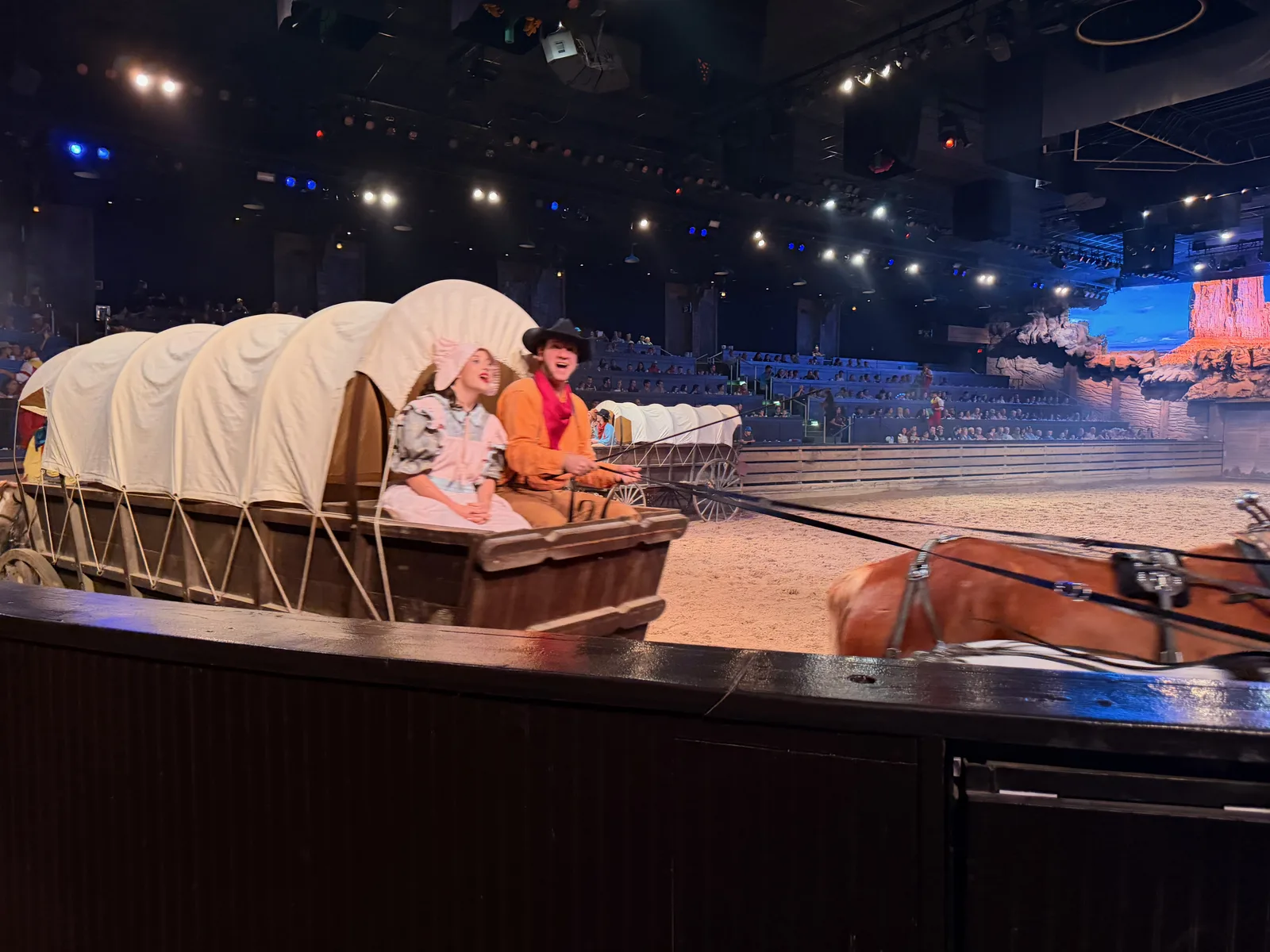 A covered wagon on the dirt arena floor during the Dolly Parton's Stampede show, stage lighting overhead