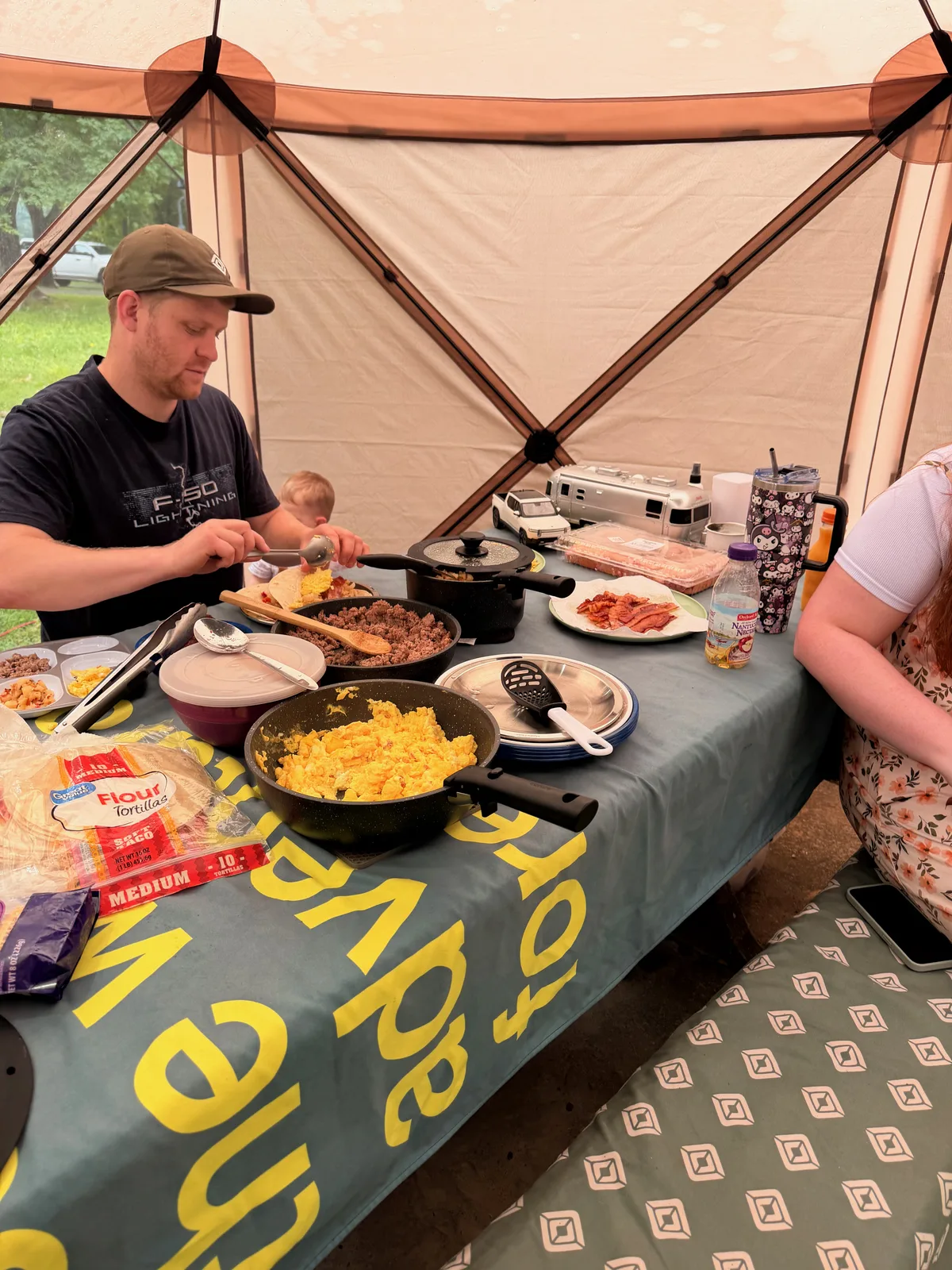 Eric eating at the camp table under the screened gazebo at Indian Point, a big potluck spread of skillets and plates across the table