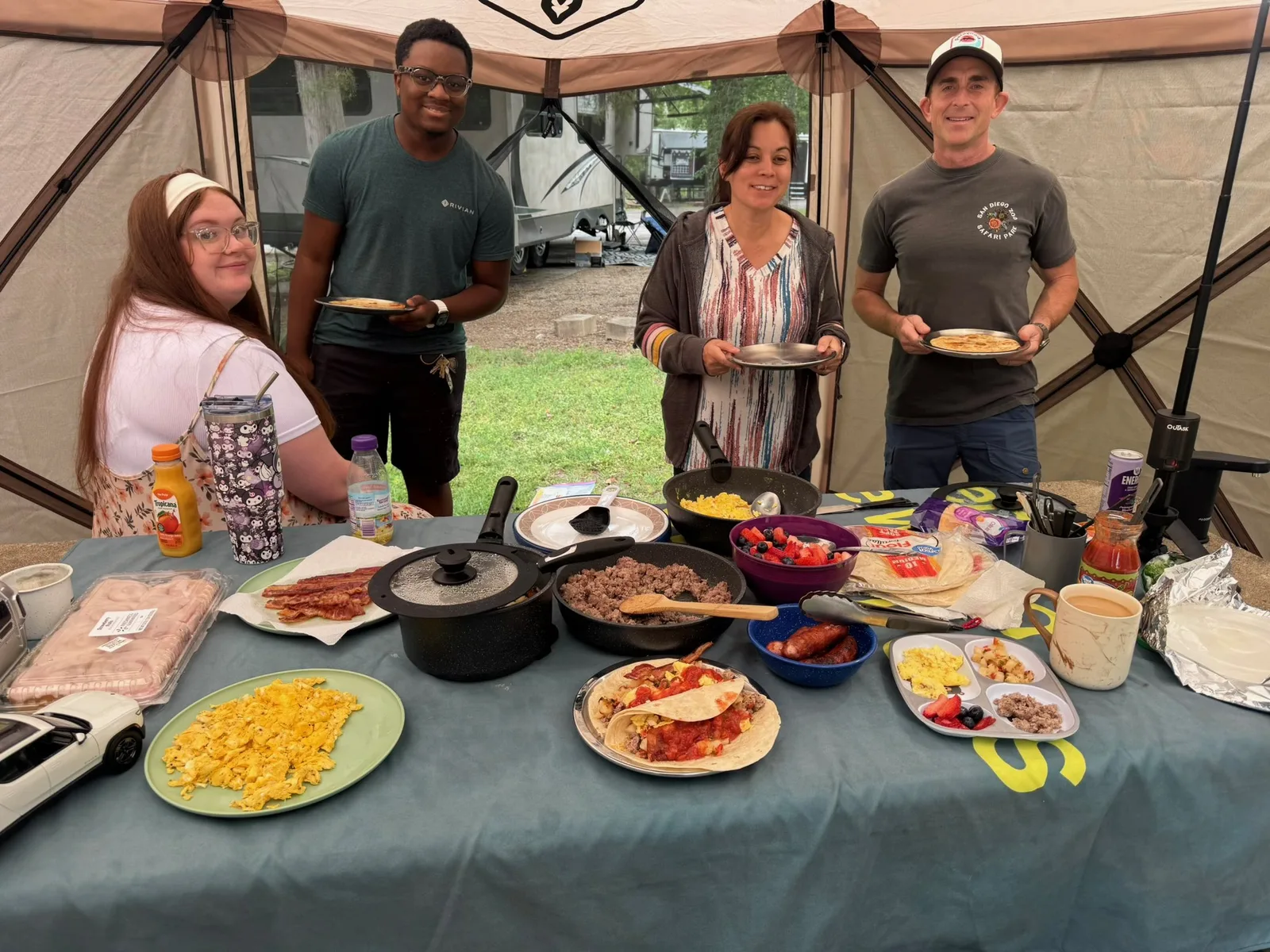 The group standing around the potluck table in the screen room at the Indian Point campsite, plates of breakfast food spread out