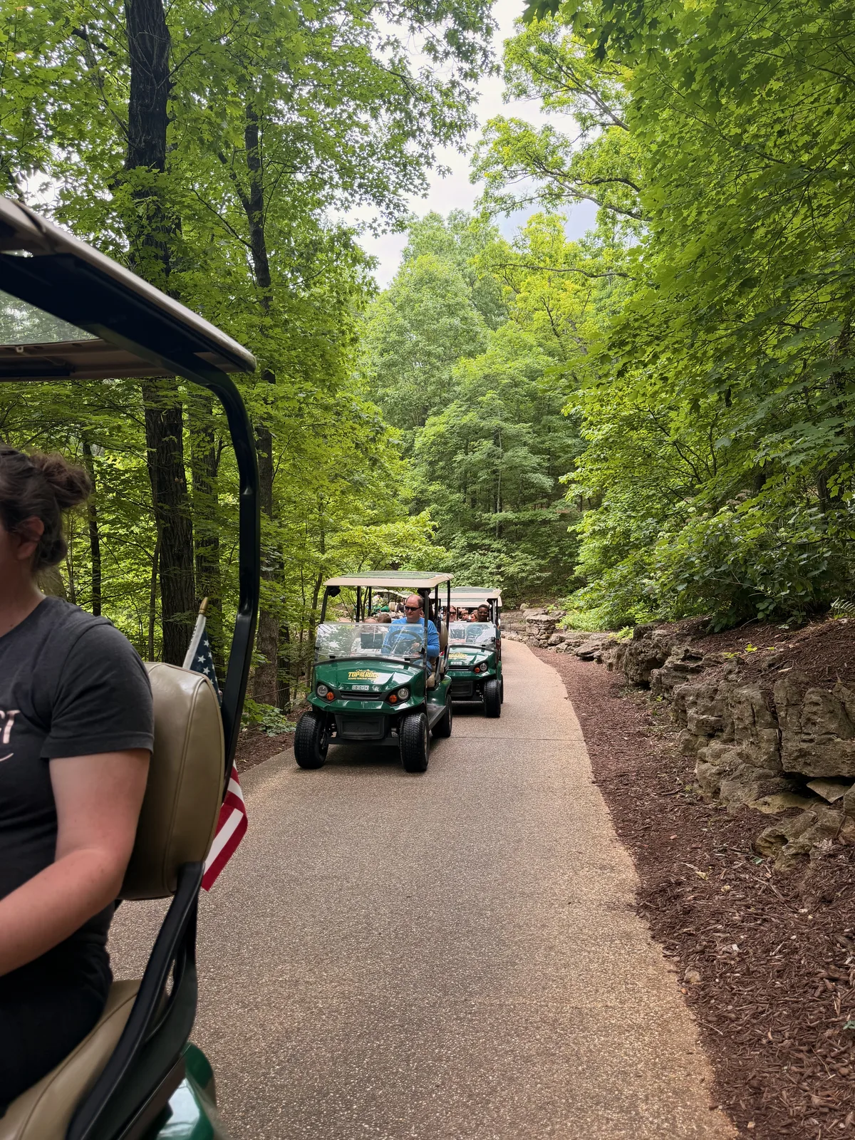 A golf cart on the paved self-drive Lost Canyon Cave trail winding between rock walls and trees at Top of the Rock