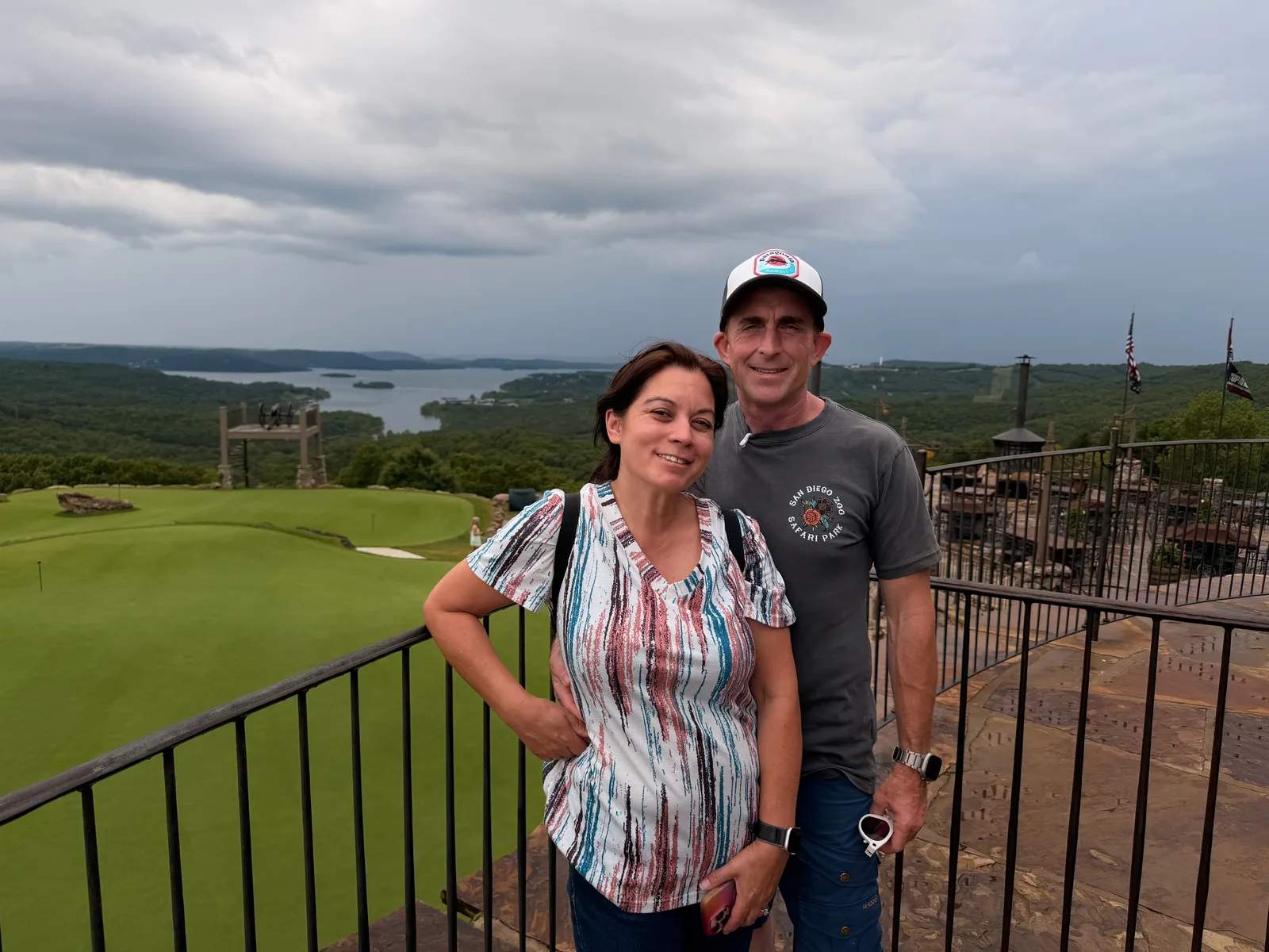 Eric and Diana on the railed terrace at Top of the Rock, the Ozark hills and Table Rock Lake spread out behind them under cloudy skies