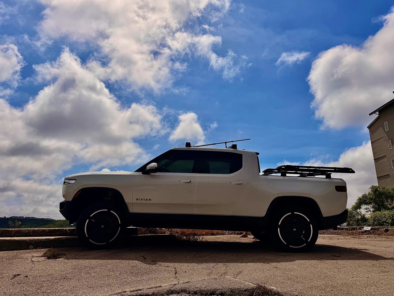 The white Rivian R1T parked at a Table Rock Lake overlook under a big blue sky with scattered clouds, the lake and wooded hills beyond