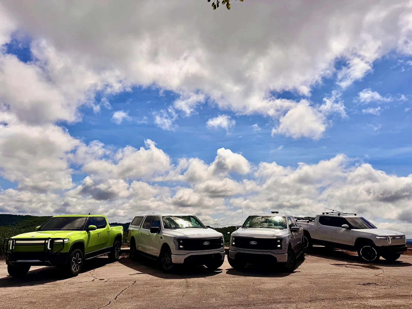 The white Rivian R1T lined up with friends' electric trucks at the Table Rock Lake overlook, the water and Ozark hills behind