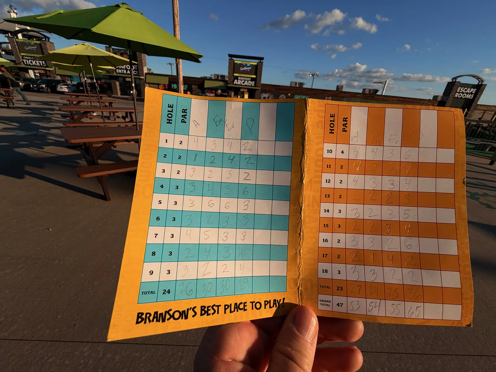 A hand holding two filled-in Bigfoot mini-golf scorecards reading "Branson's best place to play"