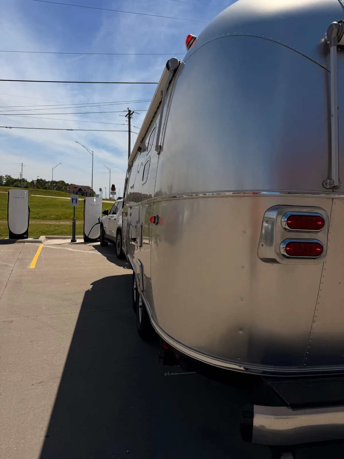 The white Rivian R1T and silver Airstream parked at the St. Robert MO Supercharger beside a red pickup, gas-station canopy behind under a bright sky