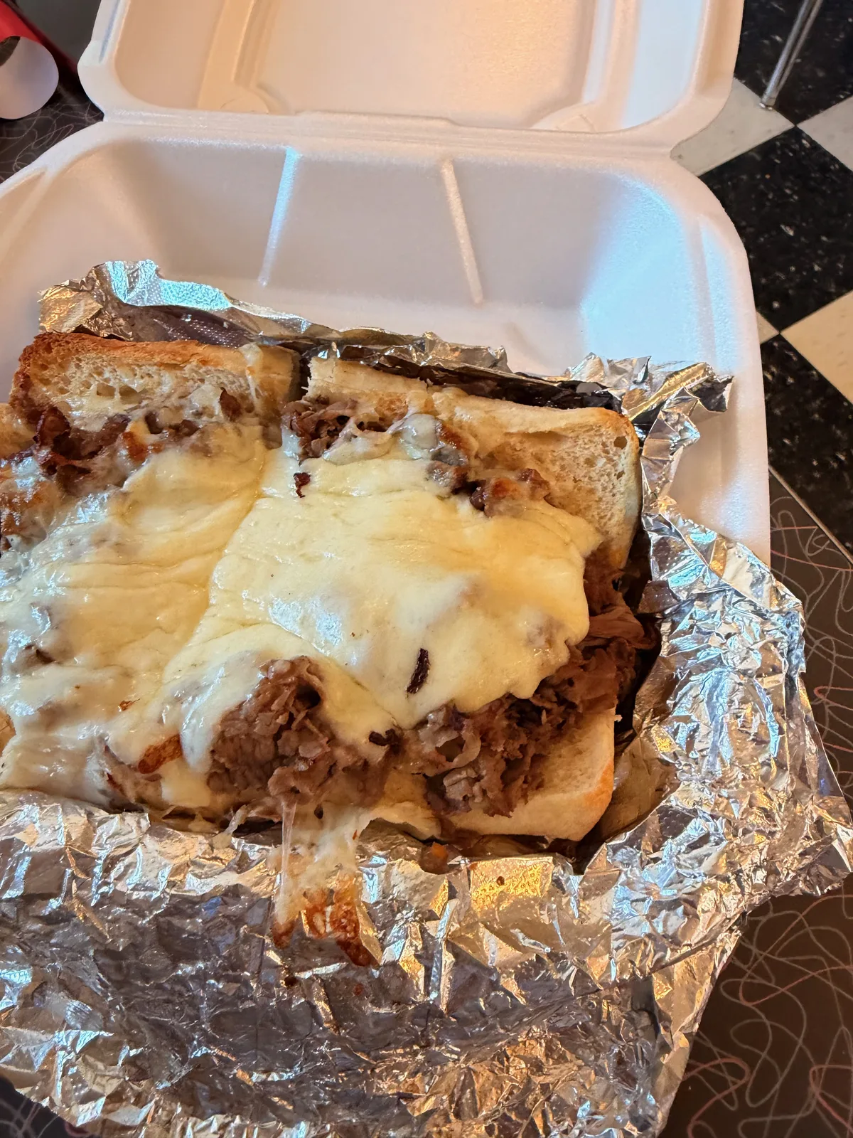 A close-up of the Orlando's Italian beef sandwich, shredded beef under a blanket of melted provolone on Italian bread in the takeout box