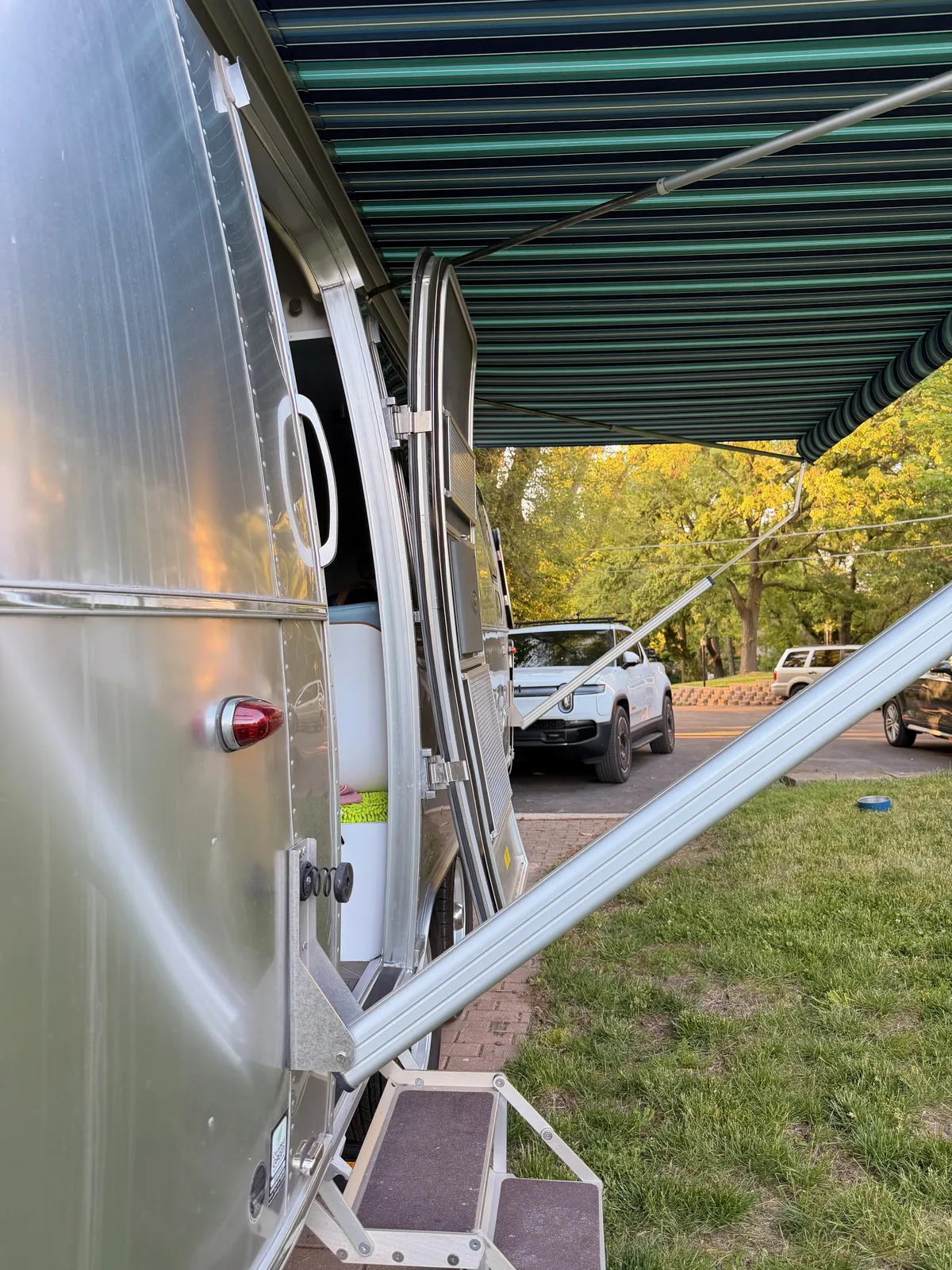 The silver Airstream parked at the friends' driveway in soft evening light, trees overhead