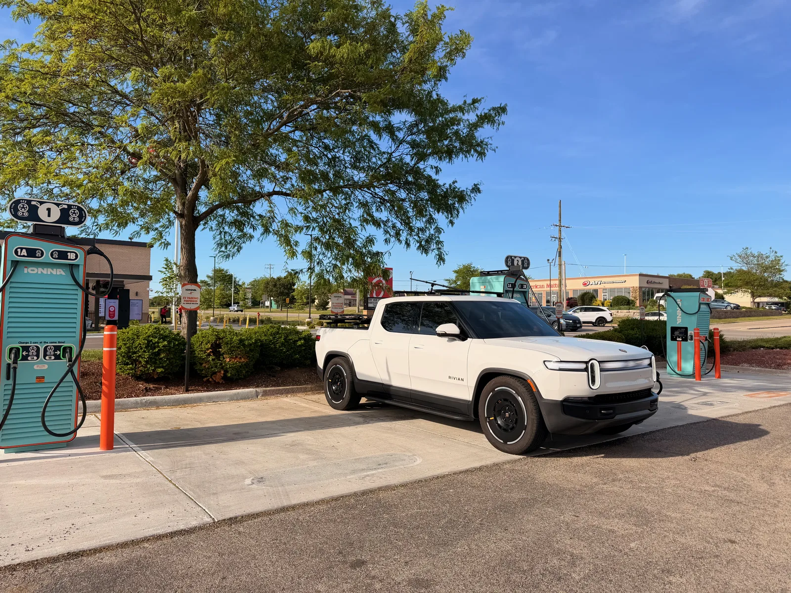 The white Rivian R1T parked at a row of tall IONNA Rechargery pedestals at the McHenry, Illinois site on a clear evening, the Casey's storefront behind