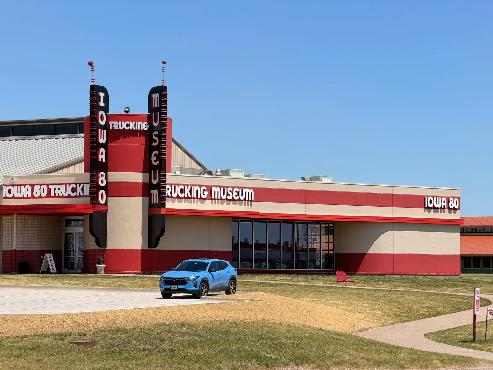 The red-and-cream exterior of the Iowa 80 Trucking Museum at Walcott Iowa, its tall vertical "Iowa 80 Trucking Museum" sign against a clear blue sky