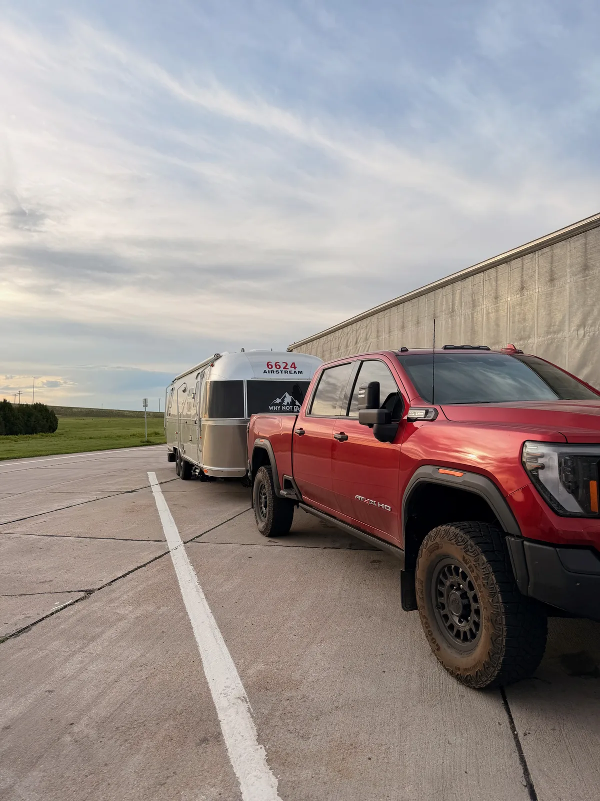 A friend's red GMC Sierra AT4 HD hitched to a polished Airstream travel trailer marked 6624 on the nose, parked at the Arriba rest area in the morning light