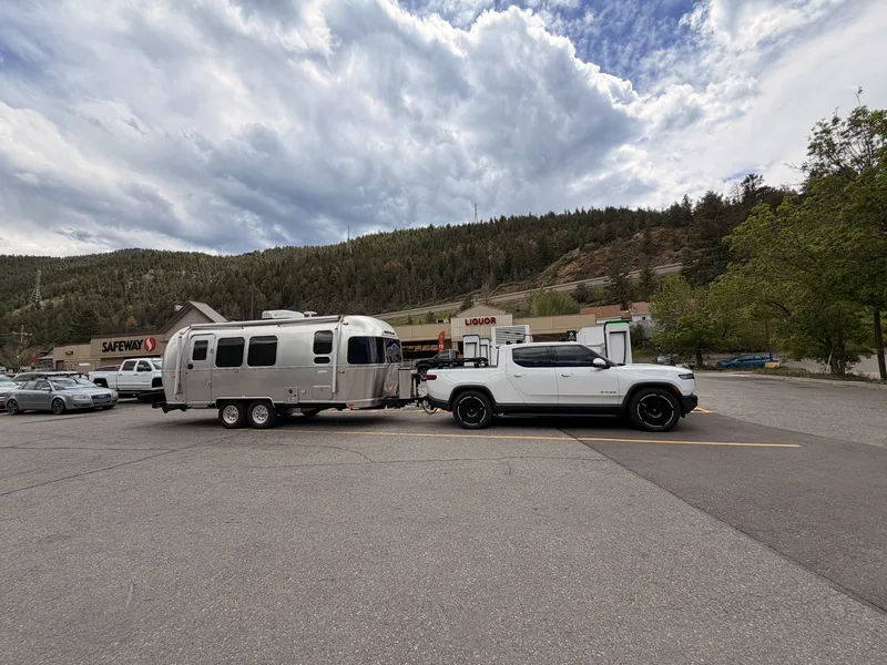 The Airstream and white Rivian R1T parked in a lot in Idaho Springs, Colorado, steep forested canyon walls behind