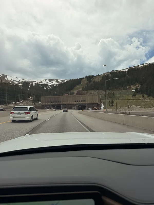 Windshield view approaching the Eisenhower-Johnson Memorial Tunnel on I-70 at the Continental Divide in Colorado, snow-streaked peaks above the tunnel portal