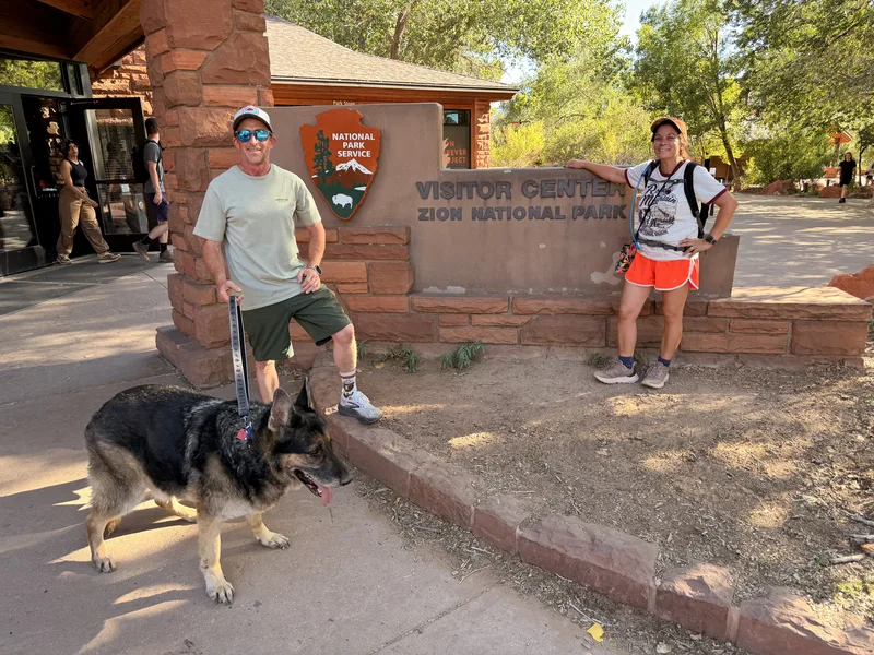 Eric, Diana, and Mission the German Shepherd at the Zion National Park Visitor Center sign in evening light