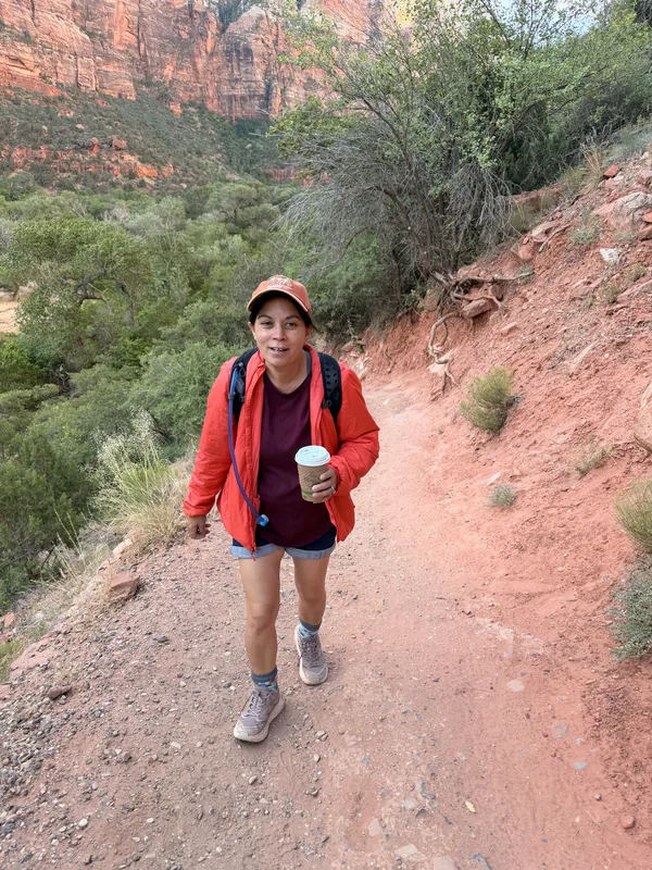 Diana in a red jacket hiking the red-dirt Lower Emerald Pools trail in Zion Canyon