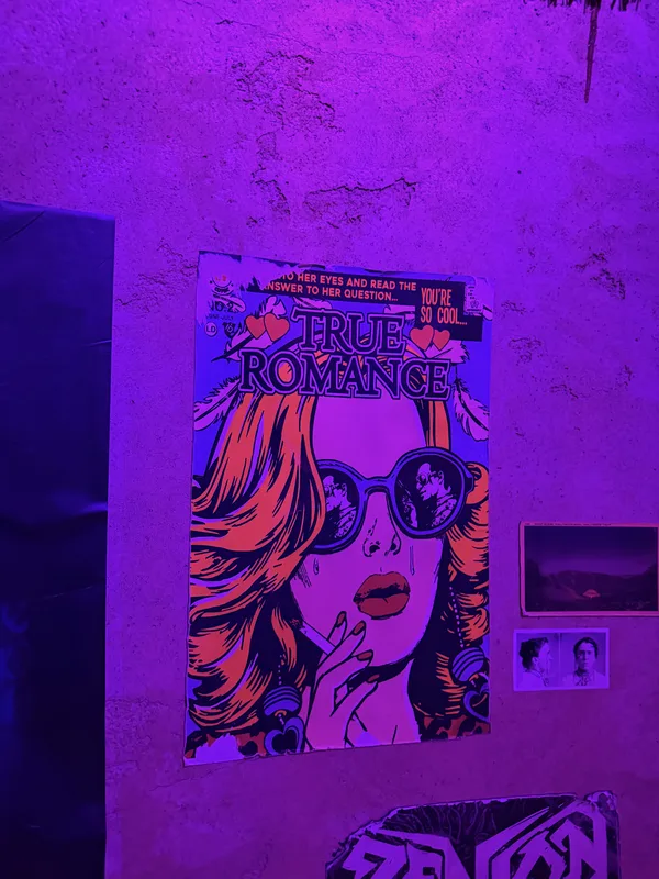 A blacklight True Romance comic-style poster glowing under ultraviolet light inside Omega Mart