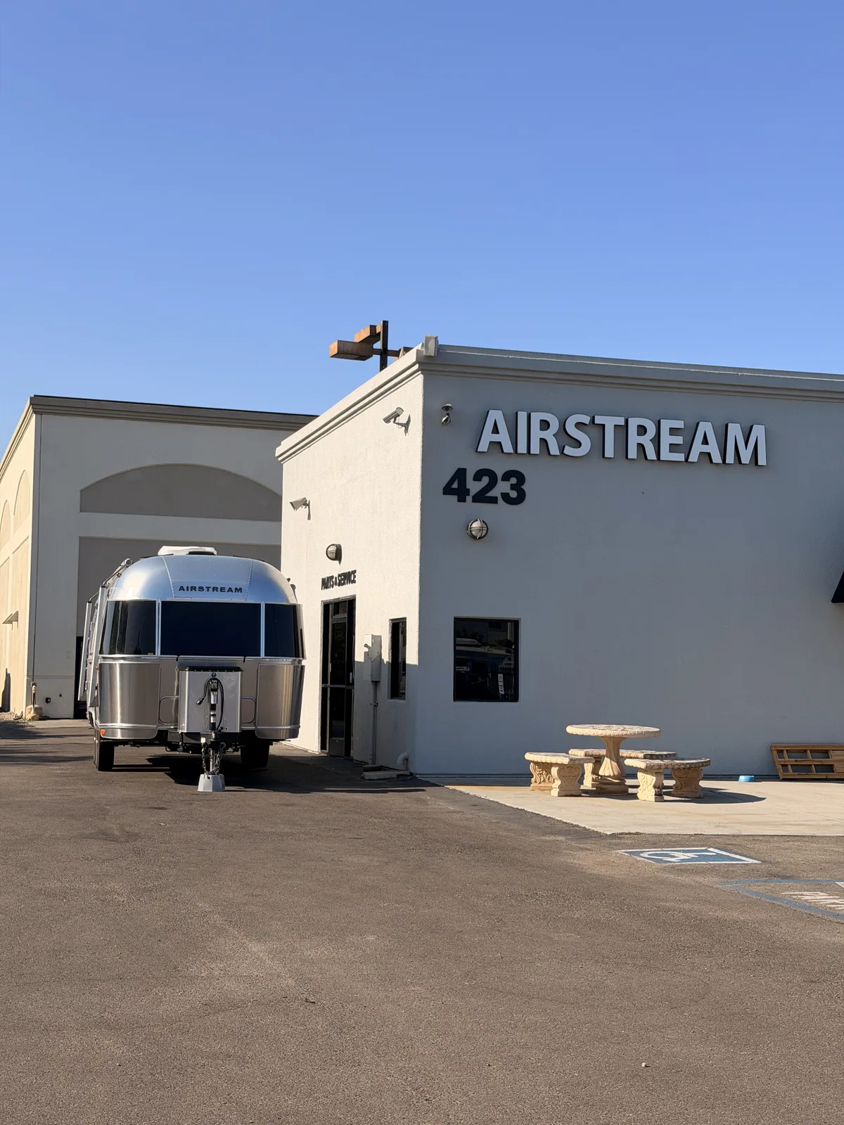 The Airstream pulled up to the Airstream of San Diego storefront, a small airplane weathervane on the roofline and a stone picnic table out front