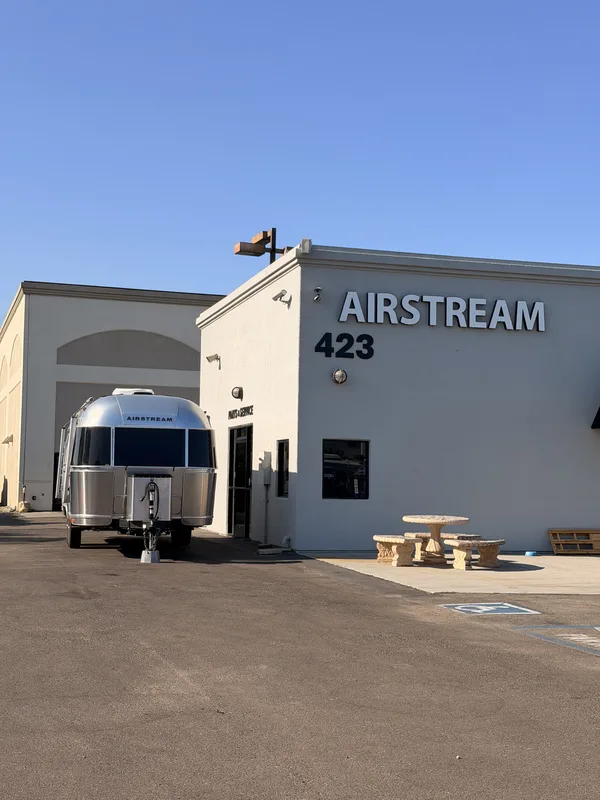 The Airstream pulled up to the Airstream of San Diego storefront, a small airplane weathervane on the roofline and a stone picnic table out front