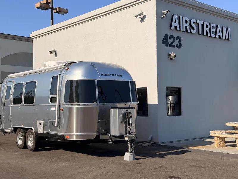 The polished 23-foot Airstream parked nose-out in front of the Airstream of San Diego service building in San Marcos under a clear blue sky, tongue jack down on the pavement
