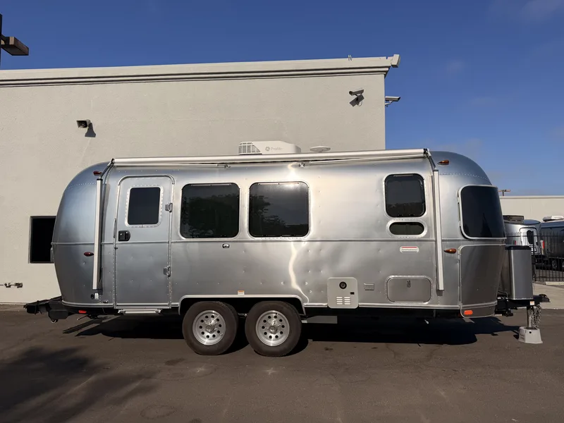 Full broadside profile of the polished 23-foot Airstream trailer parked on the dealer lot, twin axles and curbside windows in clear morning light