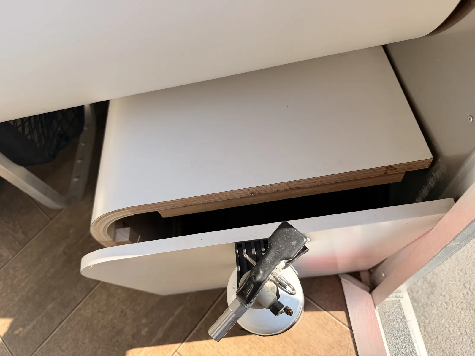 Interior detail of a white laminate panel lifting at its plywood edge near the propane tank and regulator under the Airstream cabinetry