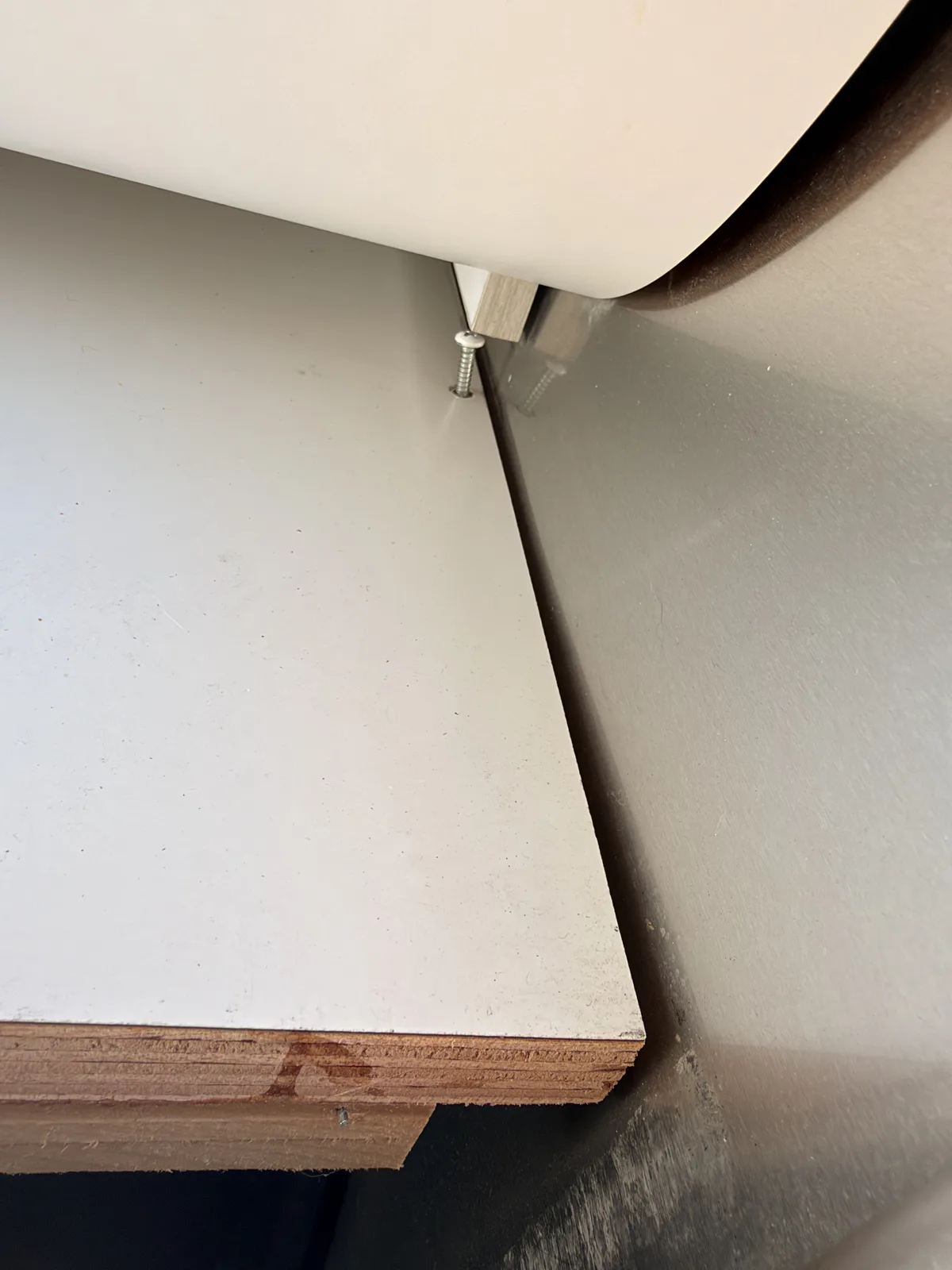 Close-up inside the Airstream of a stainless screw backing up out of a white laminate floor panel where two panels meet near the bedroom