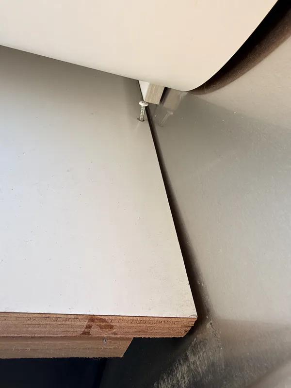 Close-up inside the Airstream of a stainless screw backing up out of a white laminate floor panel where two panels meet near the bedroom