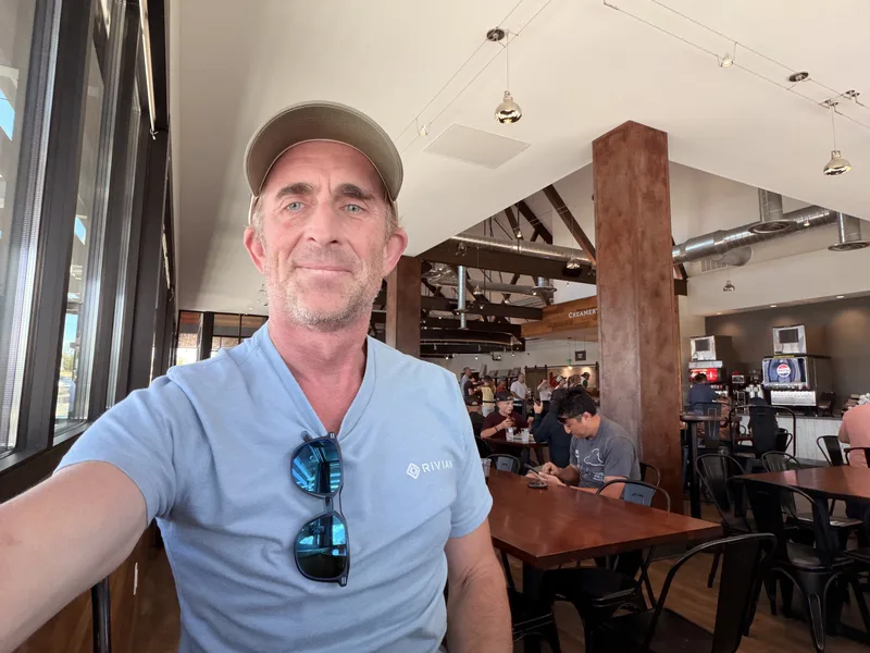 A sunglassed traveler in a Rivian shirt takes a selfie inside a busy creamery restaurant at the Beaver, Utah charge stop on the Utah Ducati Run.