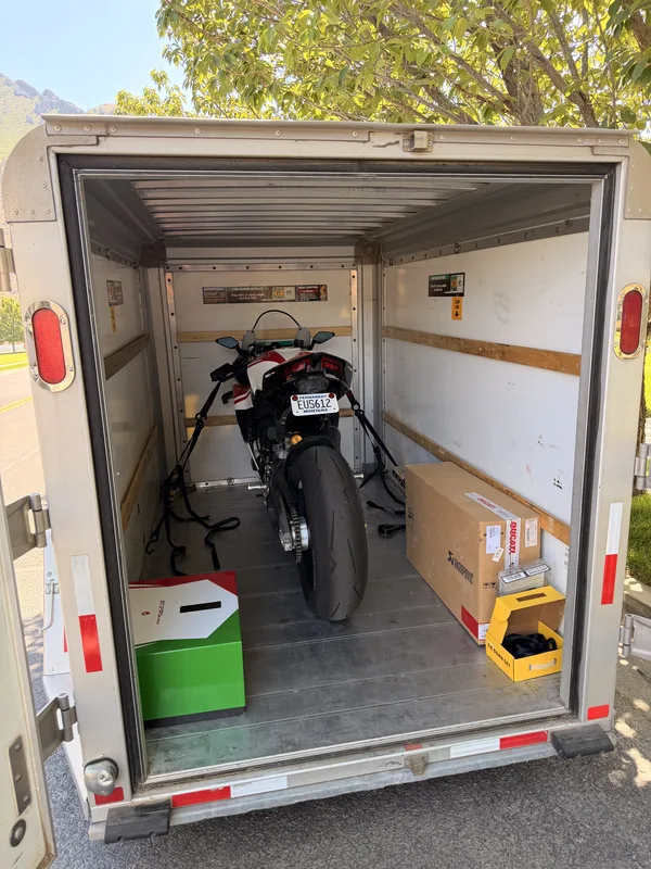 The green and white Ducati Panigale V4 strapped upright inside an open enclosed U-Haul 5x8 cargo trailer with spare parts boxes beside it, ready for the towed run home.