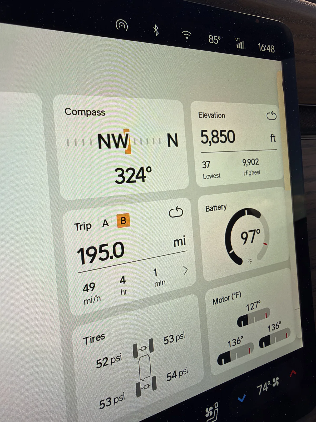 The Rivian R1T instrument display at Beaver, Utah showing Trip B 195.0 miles at 1.59 mi/kWh, 4 hours 1 minute moving time, 49 mph average, elevation 5,850 ft, motors 127 to 136°F, towing the Ducati.