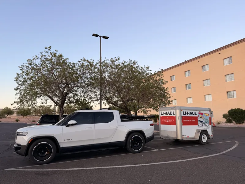 The white Rivian R1T hitched to the enclosed U-Haul cargo trailer with Chicago livery, parked at a hotel in Mesquite, Nevada at dusk, the end of the first towing day on the Utah Ducati Run.