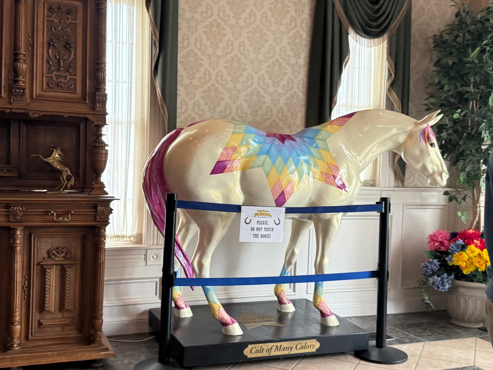 A brightly hand-painted decorative horse statue on a stand in the lobby at Dolly Parton's Stampede, rainbow colors against dark wood paneling
