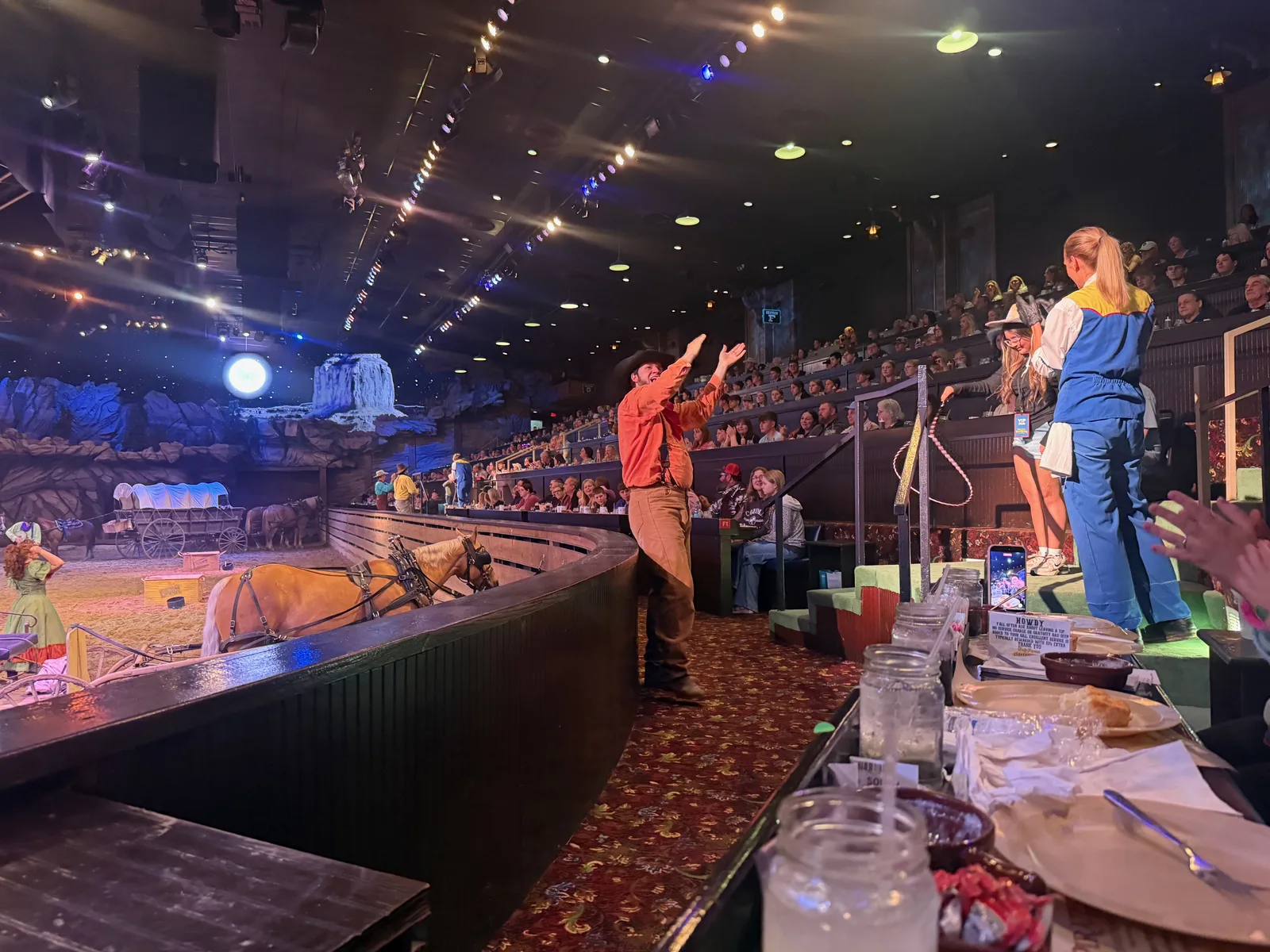 Performers and riders in action on the lit dirt arena floor at Dolly Parton's Stampede, the audience tables ringing the round