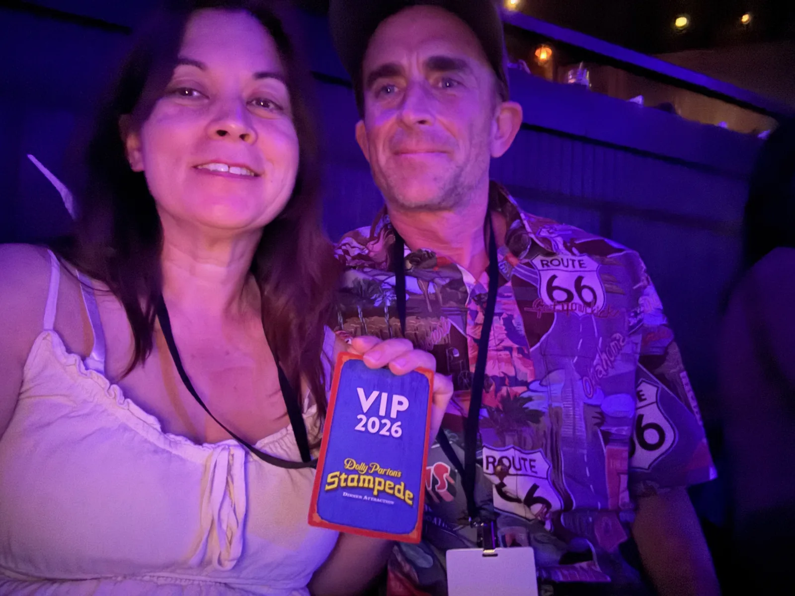 Eric and Diana in a selfie at Dolly Parton's Stampede, Diana holding a blue "VIP 2026 Stampede" lanyard card, warm arena lighting behind them