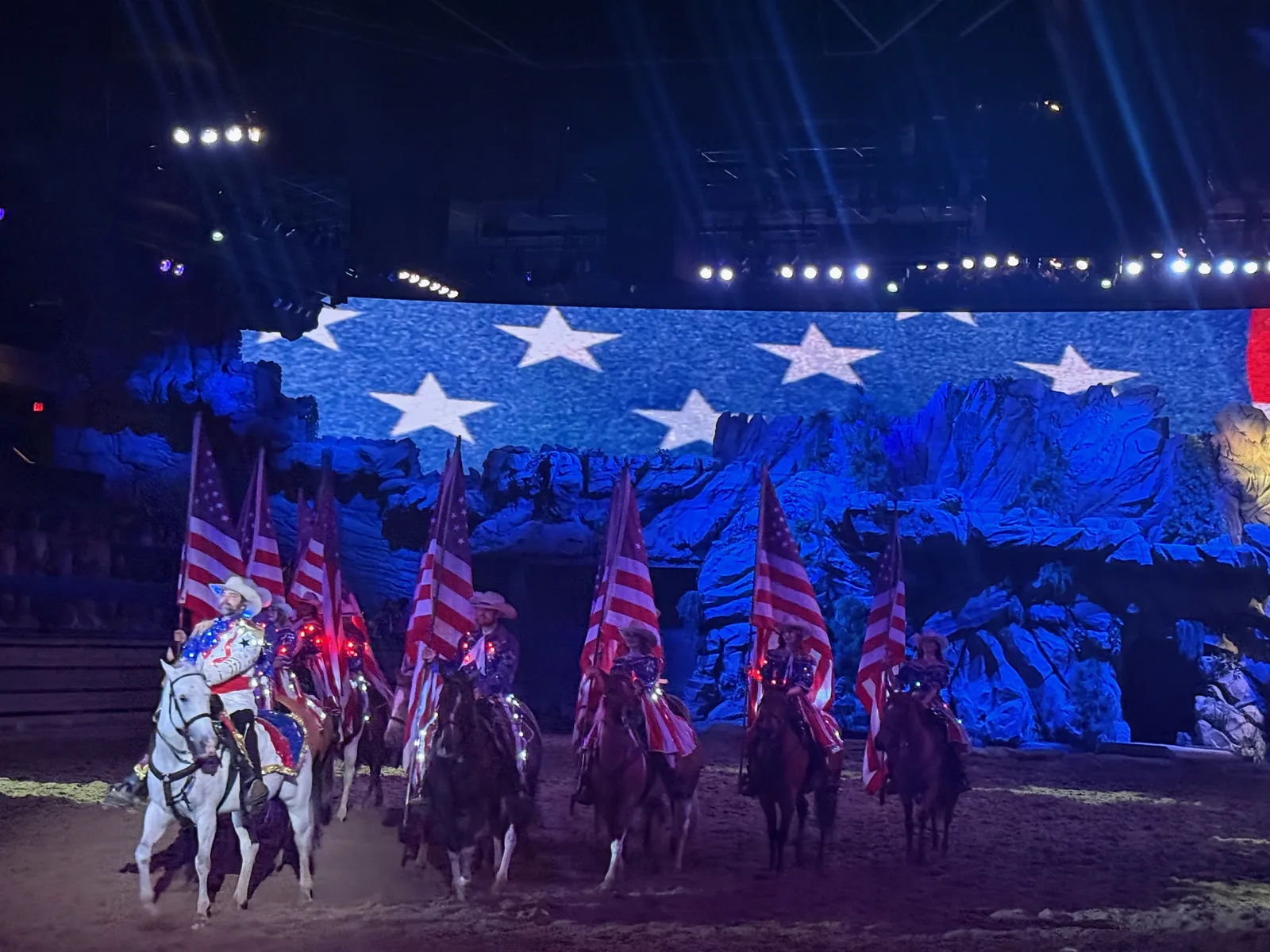 The patriotic finale at Dolly Parton's Stampede, riders carrying American flags around the dirt arena beneath an enormous Stars and Stripes