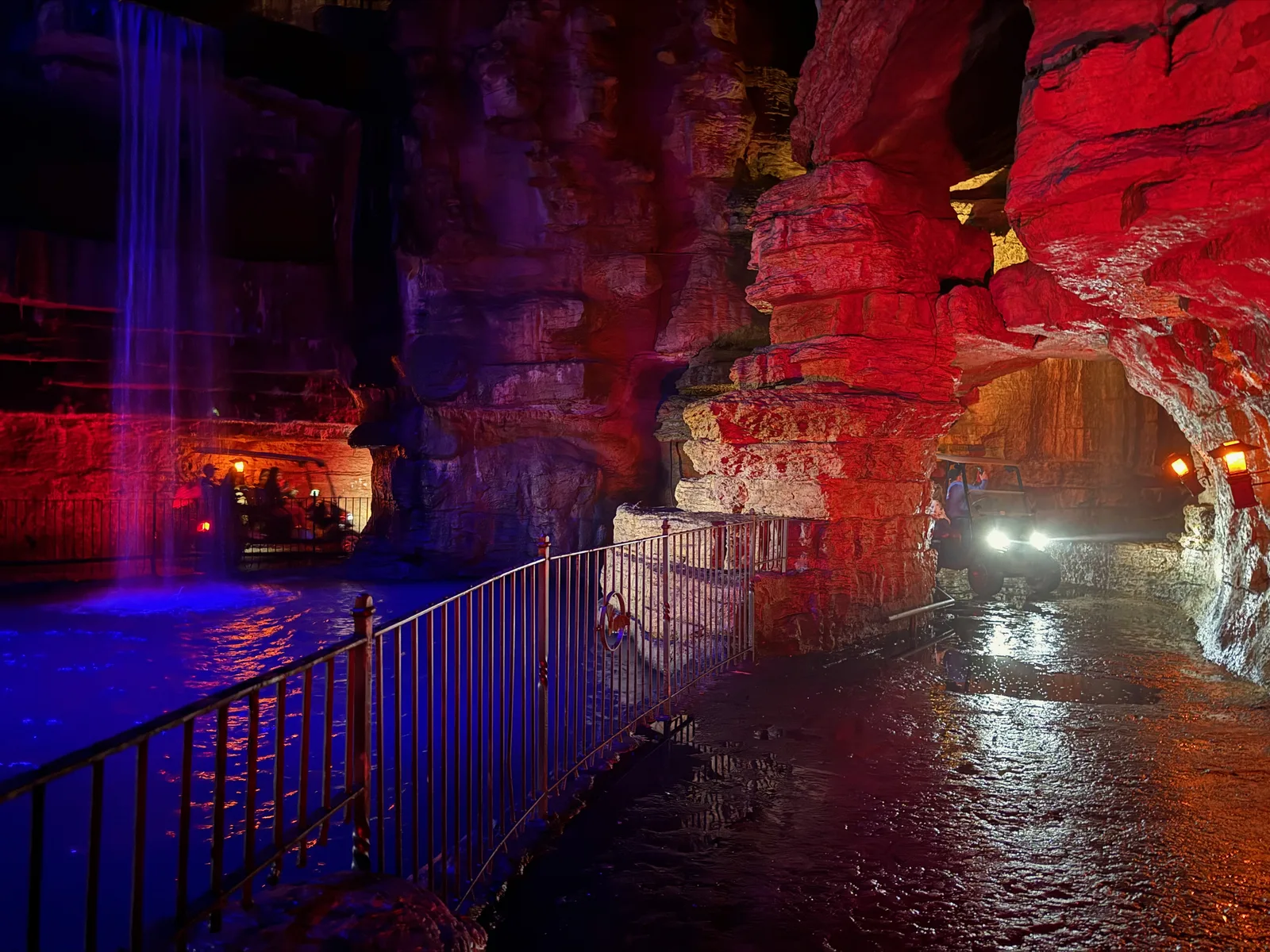 Inside Lost Canyon Cave, the man-made cavern lit deep blue and red, water on the floor and the cart path running right through the lit passage