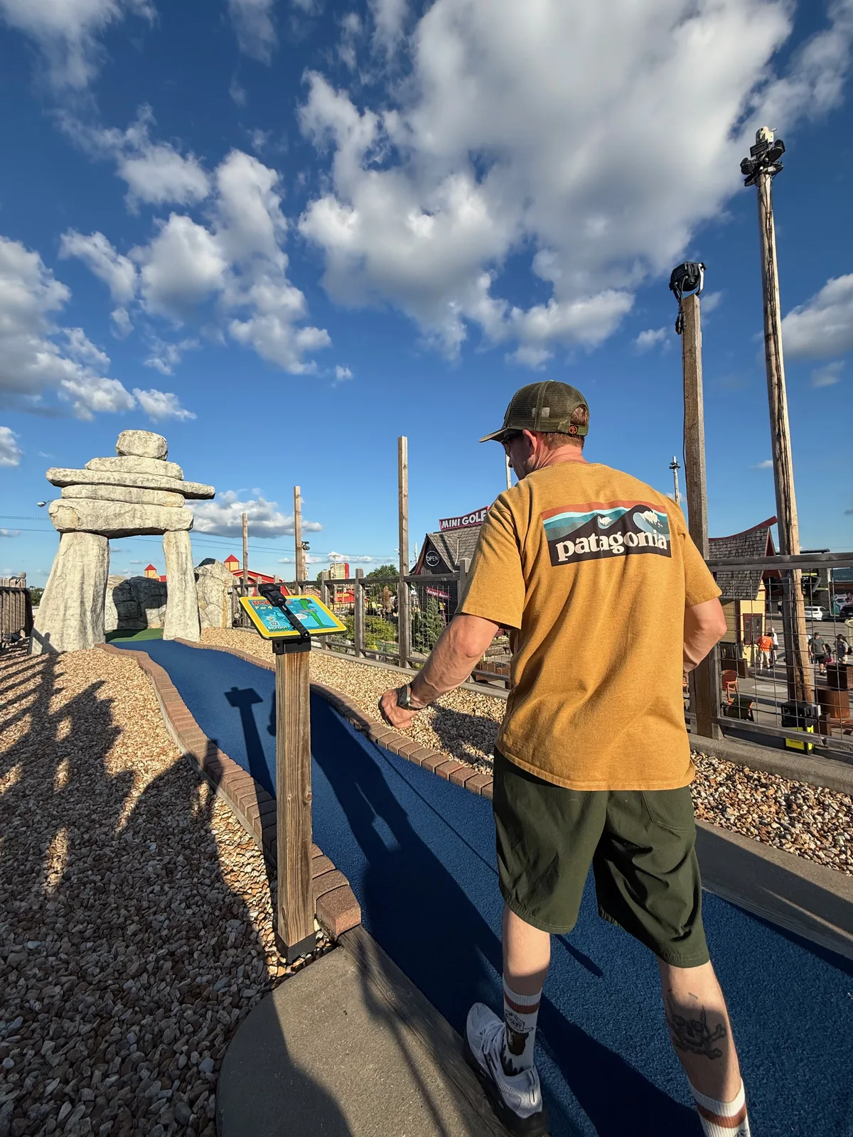 Eric lining up a putt on a mini-golf course at Bigfoot Fun Park, the tall Bigfoot tower and a bright sky behind