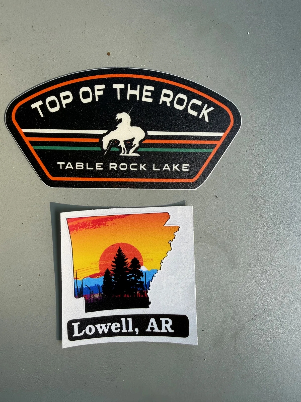 The Airstream's sticker board with a new "Top of the Rock, Table Rock Lake" patch sticker and a "Lowell, AR" sticker added to the growing trip map